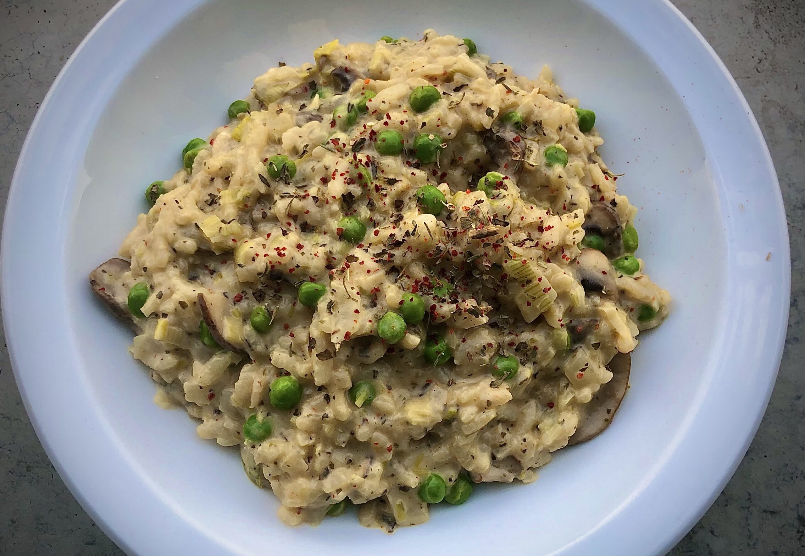 Risotto met doperwten en champignons en prei geserveerd op een wit bord