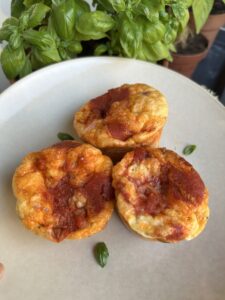 Bord met daarop drie pizza ei muffins. Op de achtergrond wat basilicum