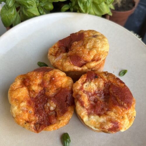 Bord met daarop drie pizza ei muffins. Op de achtergrond wat basilicum